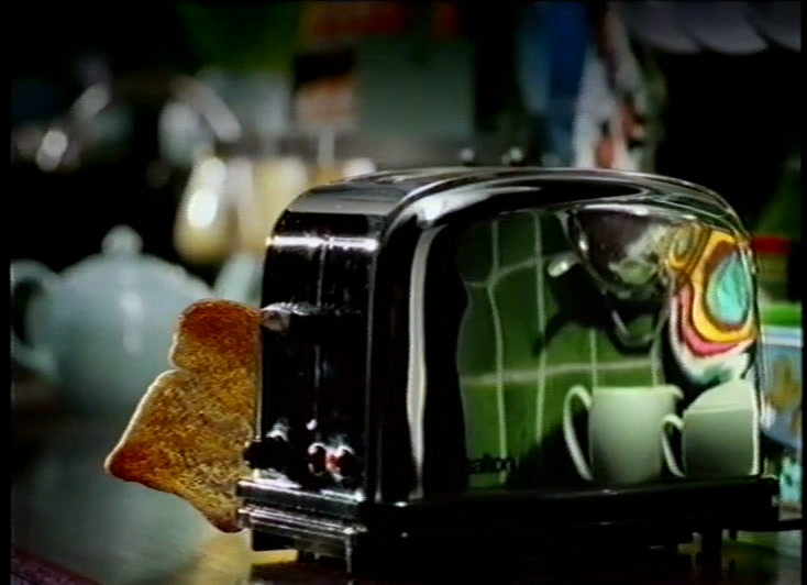 A slice topped with soft cheese and a tall frilly lettuce leaf rises from the toaster slot