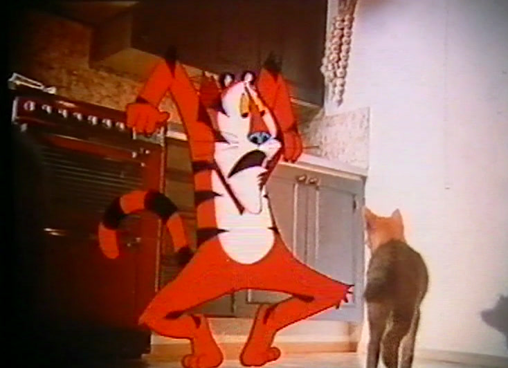 The cartoon tiger dances across a kitchen while a real cat watches from the floor.