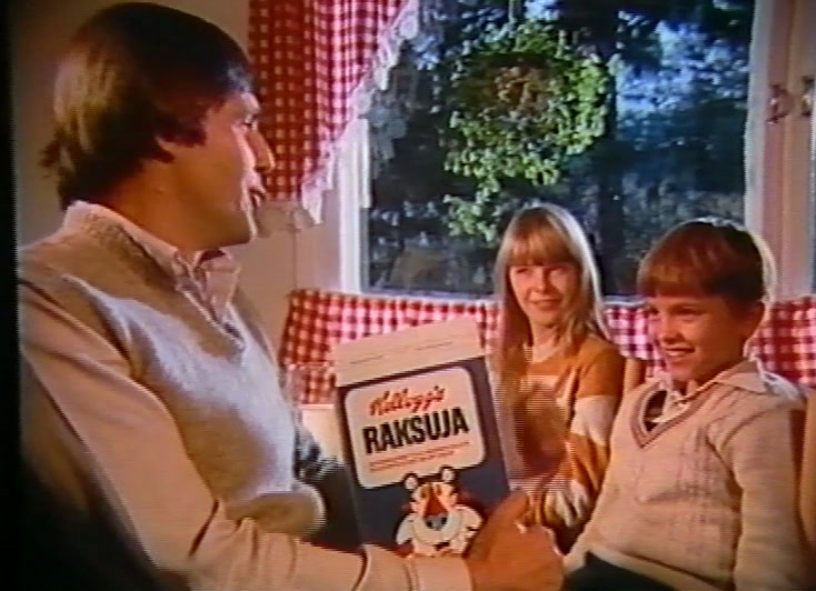 Holding the box to camera, a man in a jumper sits with two children.