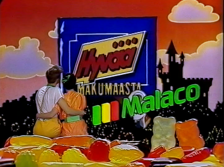 Two children sit arm in arm on a heap of jelly sweets, Malaco logo beside them.