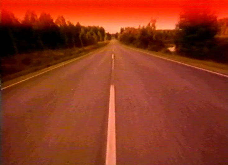 The same road in summer at dusk, red sky burning above the trees ahead.