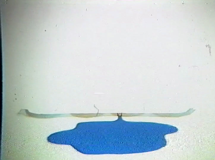 A flat paper sheet lies above a bright blue puddle on a white surface.