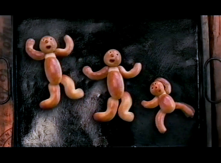 Three small dough figures with raised arms on a dark floured tray.