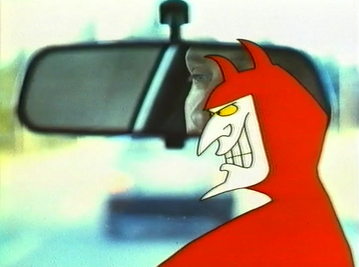 Close beside the rear-view mirror, the grinning devil; part of the driver’s face shows in the glass.
