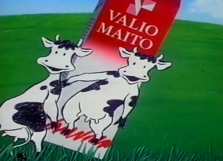 A red carton stands in the grass, one cow looking up while another dances with hooves raised.