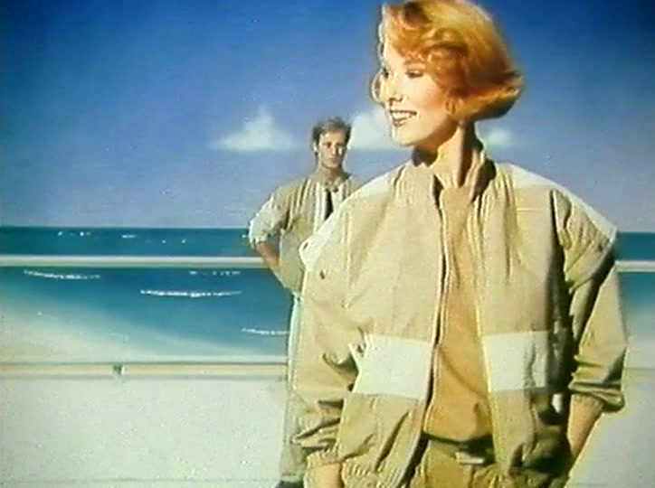 Close on a woman in a cream blouson jacket, hand on hip, hair backlit.