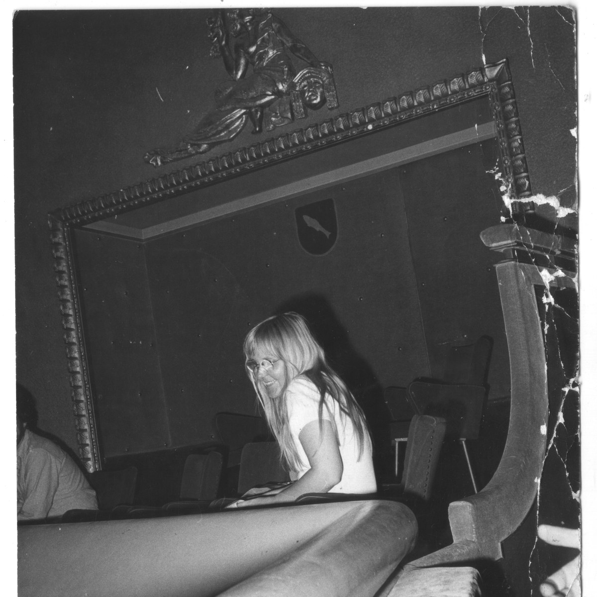 Marjut Rimminen, young, with long fair hair and glasses, turns in a theatre balcony at Annecy, smiling, the ornate proscenium above her.