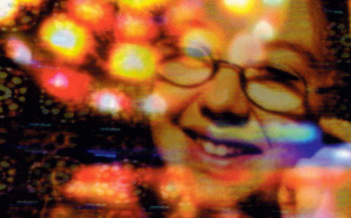 Still from Mixed Feelings, a laughing woman in glasses seen through blurred red, orange and yellow lights