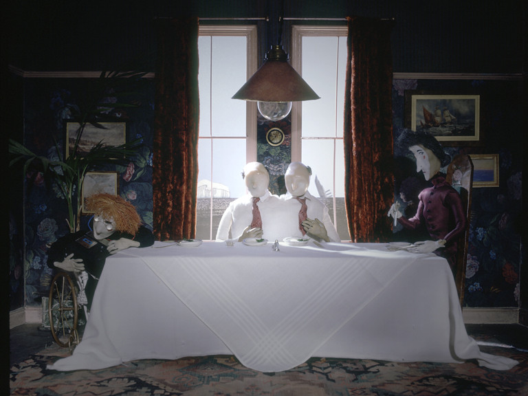 Still from The Stain — puppet figures around a dining table
